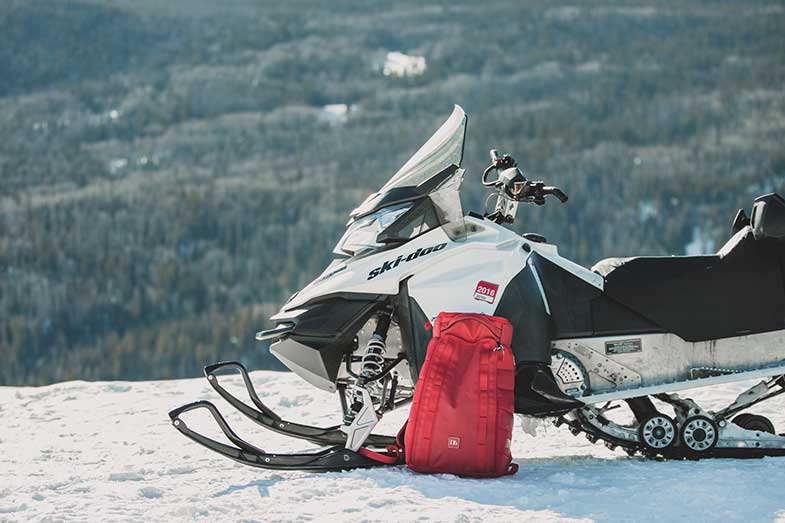 White and Black Snowmobile on a Mountain with Red Backpack