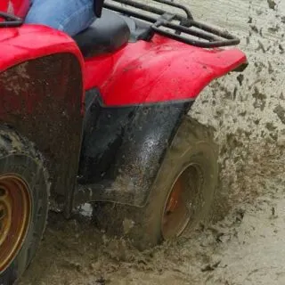 Red ATV Splashing Through Muddy Terrain