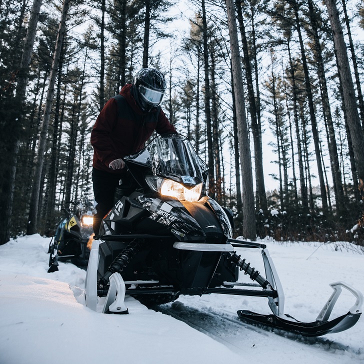 Man Riding Snowmobile Through Forest Trail